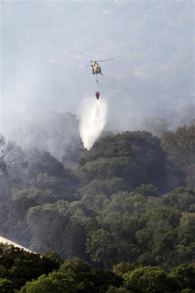 A Travis Co. Star Flight helicopter drops water on a wildfire that destroyed homes in southwest Austin, Texas on Sunday, April 17.